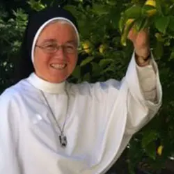 A nun holding up her hand in front of some trees.